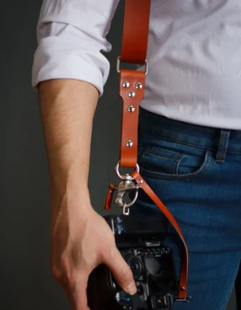 Close-up of stainless steel hardware on leather camera strap holding DSLR